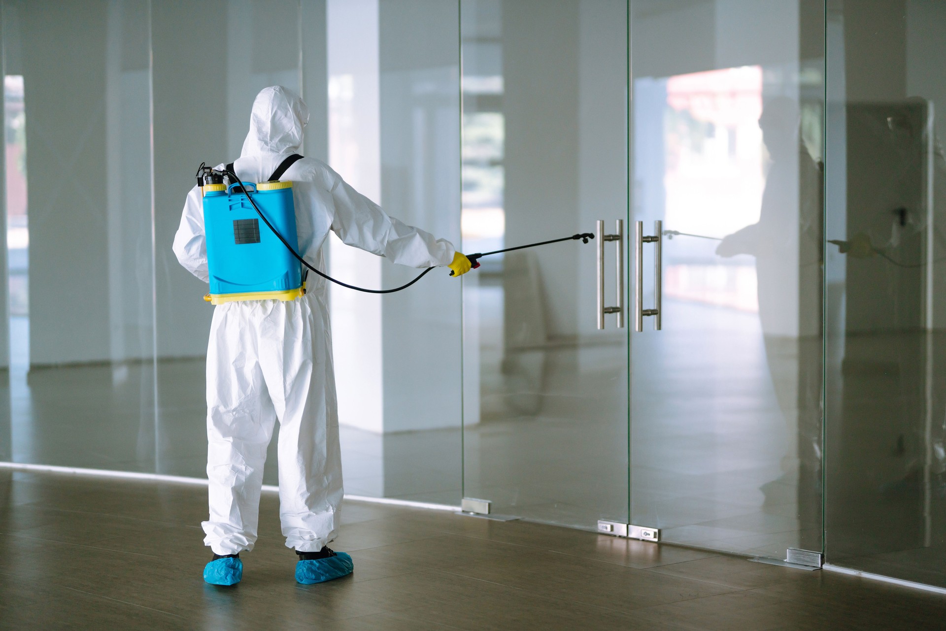 Man in Hazmat suit, protective gloves and goggles use sprayer equipment disinfect  in office. Protection agsinst COVID-19 disease.